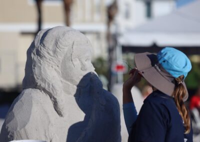 Person carving a detailed sand bust with facial features at an outdoor sculpting event.
