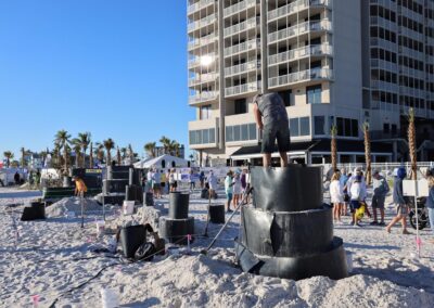 Large stacked sand molds with a person working on top at a busy beach event.