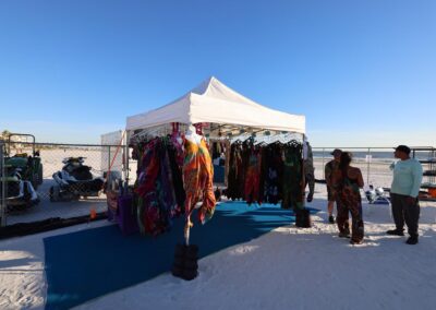 Colorful tie-dye clothing displayed under a white beach tent with people browsing nearby.