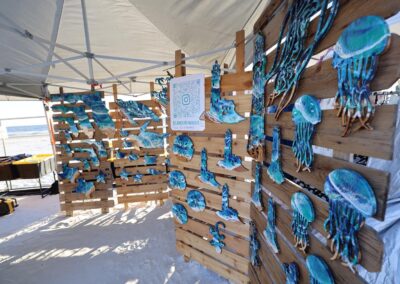 Vendor booth displaying blue and turquoise ocean‑themed wooden art on the beach.