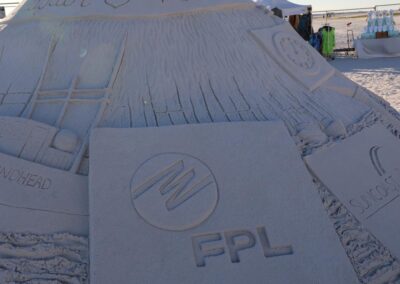 Large sand sculpture shaped like a volcano with carved logos and textured ridges.