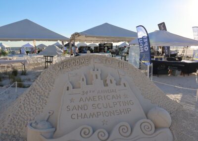 Intricate sand castle sculpture with event signage at a sunny beach festival.
