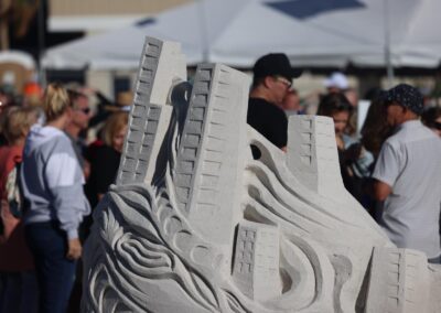Tall, detailed sand buildings rising from swirling shapes at a crowded beach event.