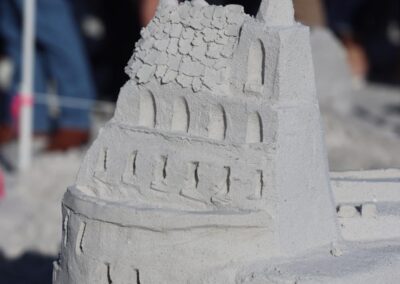 Intricate multi-level sandcastle with arched windows and textured details at a beach event.