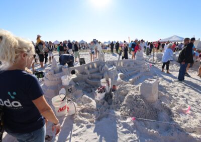 Elaborate sandcastle with towers and arches surrounded by tools and onlookers.