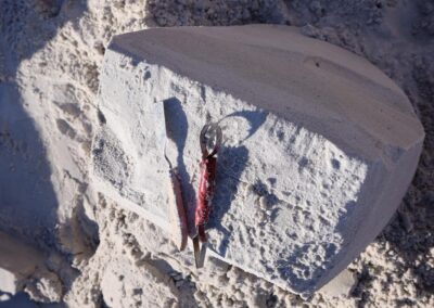Two sculpting tools resting on a square block of compacted sand on a sandy worksite.