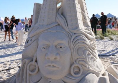 Intricate sand sculpture of a human face with earrings, flowing hair, and a tall headdress.