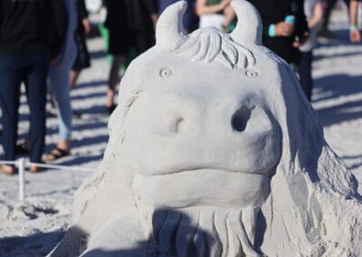 Detailed sand sculpture of a horned creature with a broad nose and textured mane on the beach.
