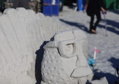 Sand sculpture of a stylized creature with glasses, mustache, and textured patterns at a beach event.