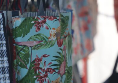 Tote bags with tropical and patterned designs hanging on display at a market stall.