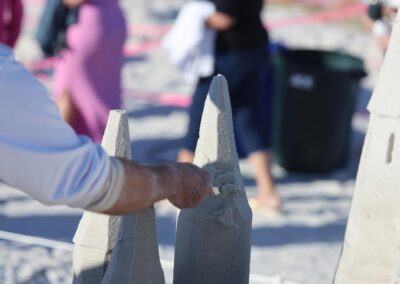 Person carving a smooth, tall sand tower during a beach sand sculpting competition.