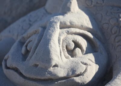 Detailed sand sculpture of a dragon’s face with carved eyes, scales, and a wide smile.