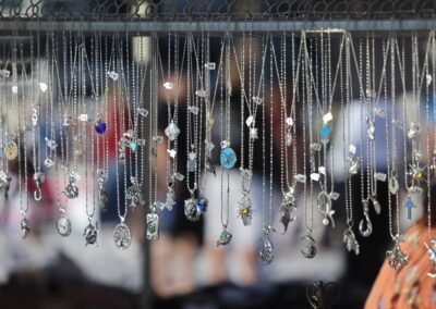 Assorted silver necklaces with decorative pendants hanging from a rack at an outdoor market.