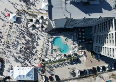 Aerial view of a hotel pool and a crowded beach event with tents and sand sculptures.