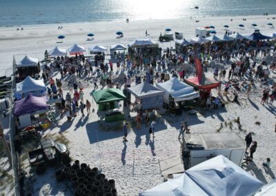 Beach festival with rows of colorful tents and crowds walking near the shoreline on a bright day.