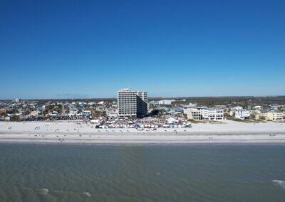 Aerial view of a coastal town with a large beach gathering, tents, and crowds near a tall central building.