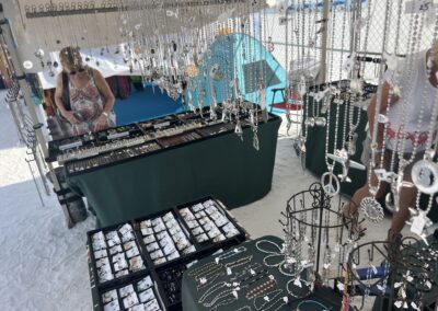 Beachside jewelry stall with trays of rings and necklaces under canopy, shoppers browsing.
