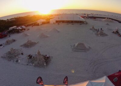 Sand sculptures across a beach at sunset with tents, people, and long warm shadows.