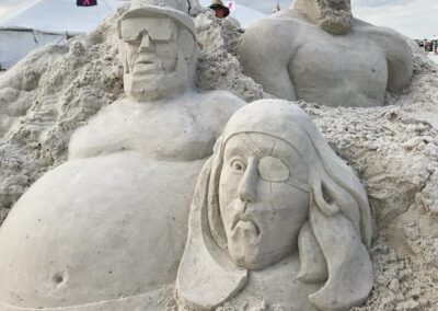 Three detailed sand sculptures of human‑like figures with tents and flags behind them.
