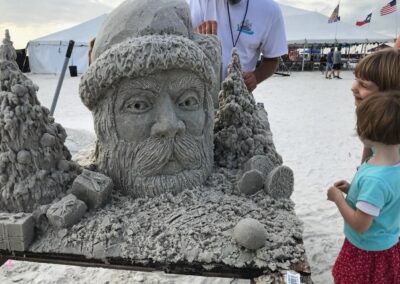 Children viewing a detailed sand sculpture of Santa surrounded by holiday‑themed sand elements.