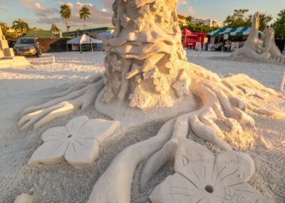 Intricate sand sculpture of a woman surrounded by large flowers and flowing organic designs in warm sunlight.