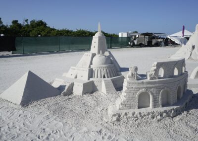 Sand sculptures of a pyramid, domed temple, and partial colosseum at a beach event.