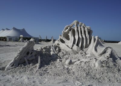 Intricate sand sculpture resembling curved rib or fossil structures under bright sun at a beach event.