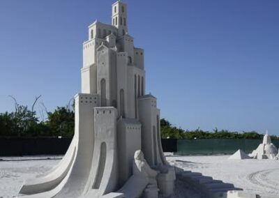 Tall geometric sandcastle with smooth curves and sharp towers displayed at a beach sculpting event.