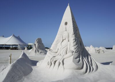 Tall sand sculpture of a seated figure with flowing lines and surrounding artistic structures.