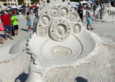 Intricate sand sculpture with layered circular patterns and a stylized bird figure at a beach festival.