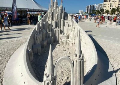 Intricate sand castle sculpture with tall spires and arches displayed at a beach festival.
