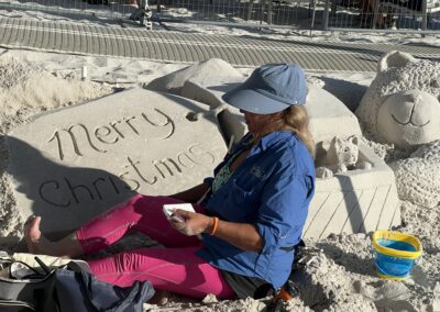 Person sculpting a sand display featuring a teddy bear, a cat, and a “Merry Christmas” tag.