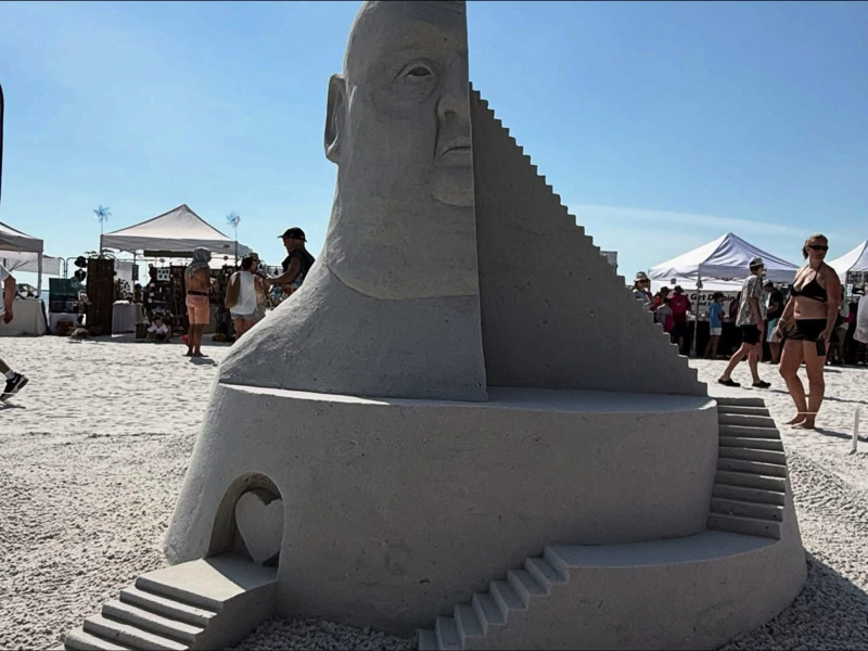 Large sand sculpture of a human head split by staircases, with multiple steps and carved architectural details.