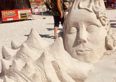 Large sand sculpture of a calm face with flowing textured details at a beach art festival.