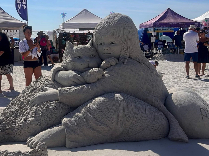 Sand sculpture of a child hugging a large cat, showing detailed textures in the hair, clothing, and fur.
