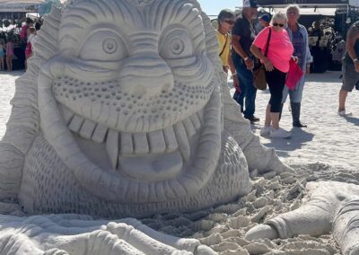 Detailed sand sculpture of a grinning creature with large teeth and clawed hands emerging from the sand.
