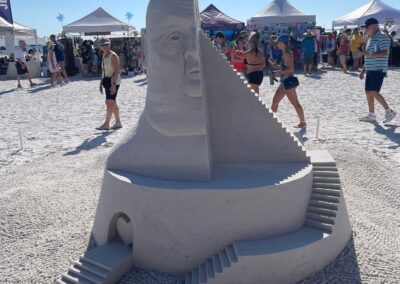 Tall sand sculpture featuring a carved face, winding staircases, and a small figure at the top.