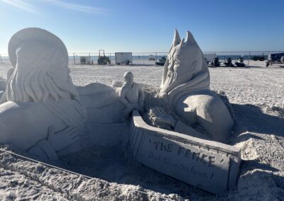 Sand sculpture of two opposing figures with a small person sitting on a fence between them.