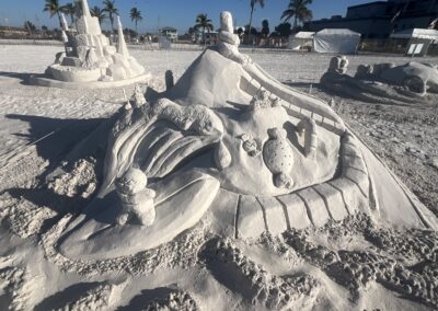 Whimsical sand sculpture with a gingerbread figure and candy shapes at a beach event.