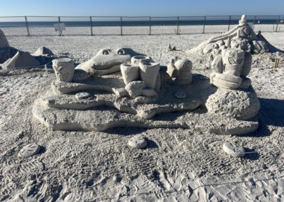 Sand sculpture featuring a large frog‑like figure surrounded by tiki‑style faces and carved circular medallions.