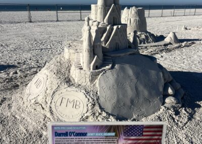 Sand sculpture of a detailed castle with “Oh the Places You’ll Go!” engraved, displayed with an artist sign in front.