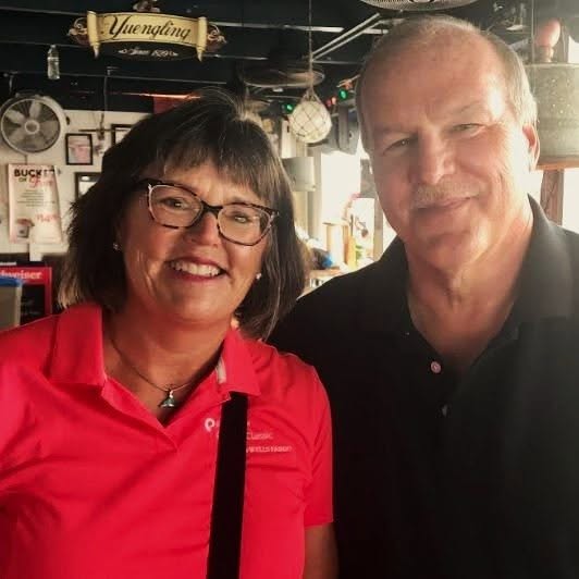 Woman in red polo with glasses and man in black shirt smiling together at bar/restaurant.